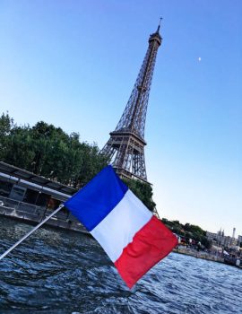 A French flag flying from the rear of a tour boat flutters in the wind on the Seine River with the Eiffel Tower in the background in Paris, France.  The camera axis is slightly tilted.