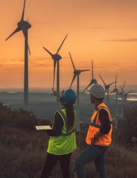 Young electrical engineer woman and business man standing in front of wind turbines checking and working about technical problems and writes the results of measurements with laptop pc in wind power plant electric energy station. xxxl size taken with canon 5d mIV